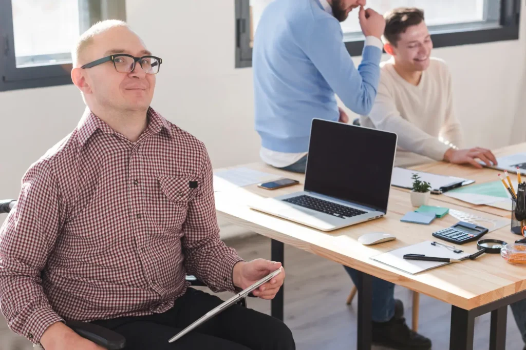 Trabajador con discapacidad en entorno profesional colaborando con su equipo en oficina, ejemplo de centro especial de empleo